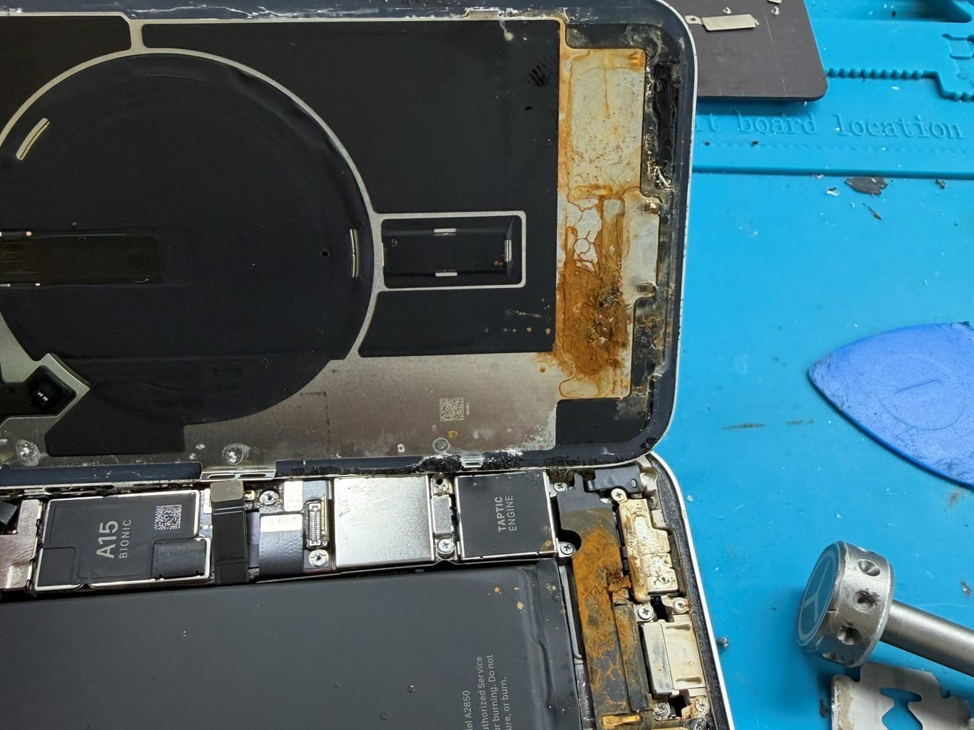 Interior de un iPhone abierto con corrosión anaranjada por líquido junto a la batería y el puerto de carga