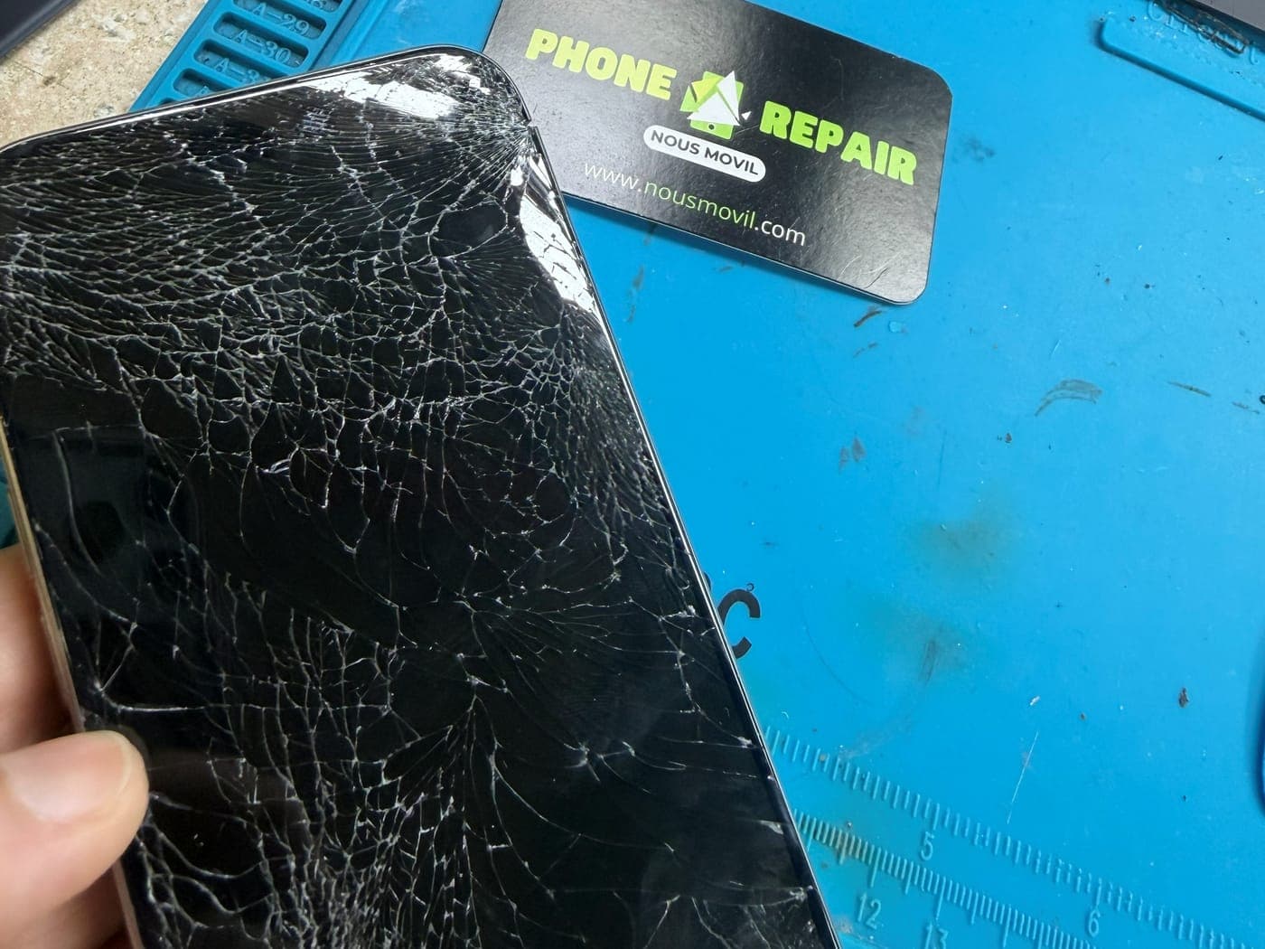 iPhone con la pantalla completamente rota sobre la mesa de trabajo de Nous Movil Repair